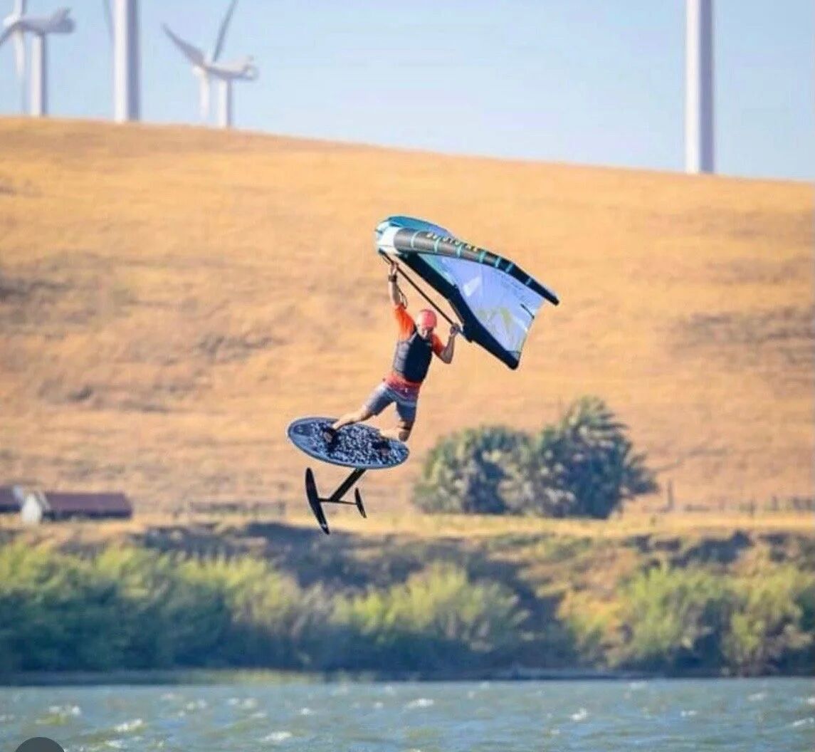Wing foiling on a Vince Broglio board with wind turbines in background